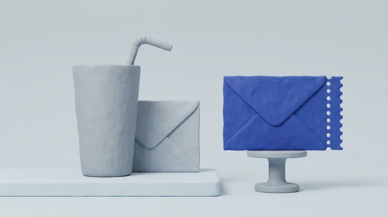 A tall grey glass with a drinking straw standing in it and an envelope tucked behind, beside a single blue envelope with a perforated edge on a small pedestal